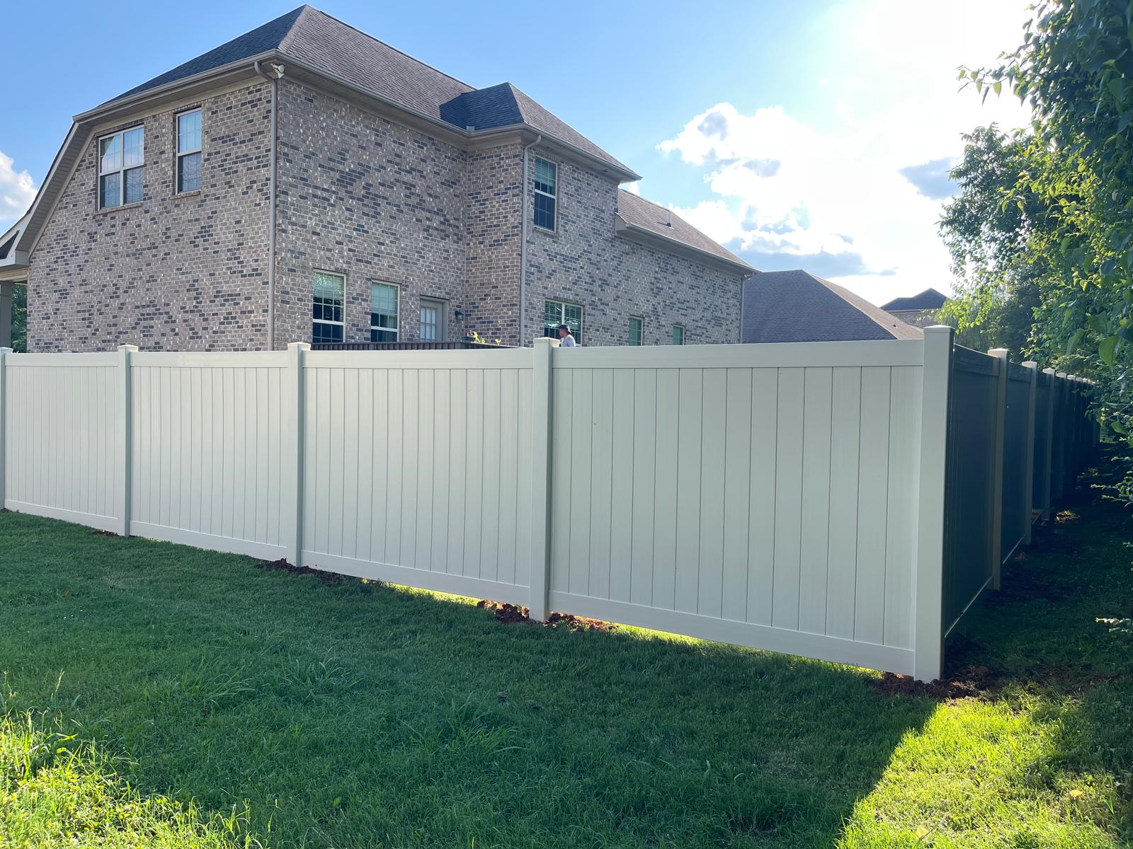 Tan vinyl privacy fence around a brick home
